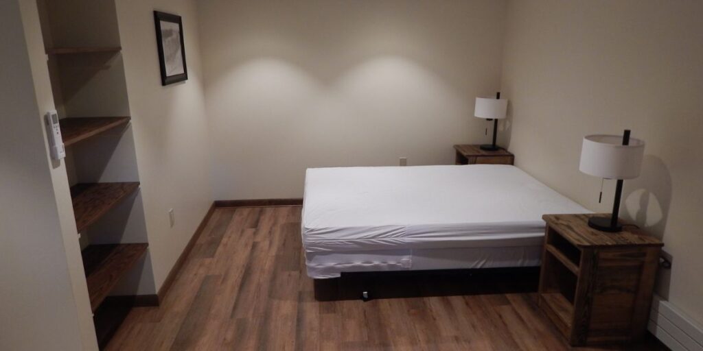 A small bedroom with a metal bed frame and a nightstand, providing durability and cost-effectiveness for shelters.