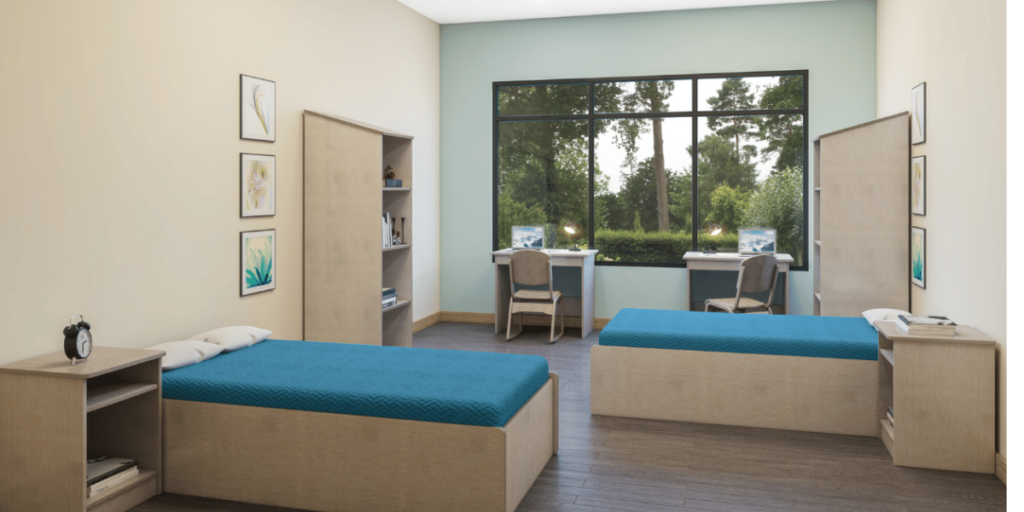 A room featuring two beds and a desk, emphasizing the importance of bed bug-proof furniture in healthcare settings.