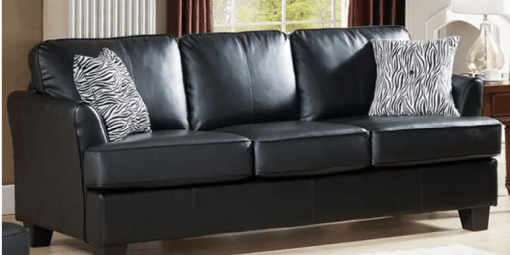 A black leather sofa adorned with pillows, accompanied by a cozy rug, enhancing the comfort of any living space.