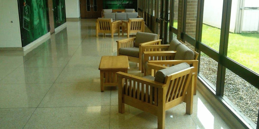 A long hallway featuring wooden chairs and tables, designed to create a warm, home-like atmosphere in healthcare settings.