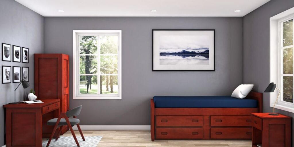 A clean bedroom featuring a bed, desk, and drawers, designed for hygiene and infection control in healthcare settings.