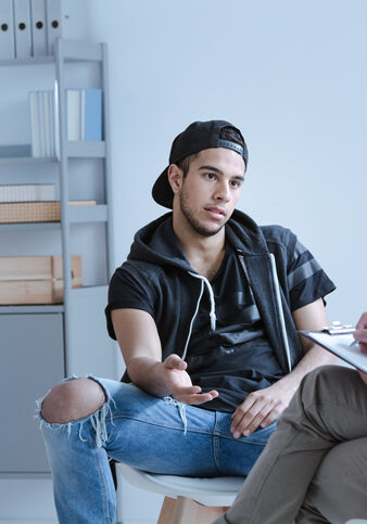 A rebel teenage boy with behavioral problems and criminal past talking to a psychotherapist in a juvenile detention center.